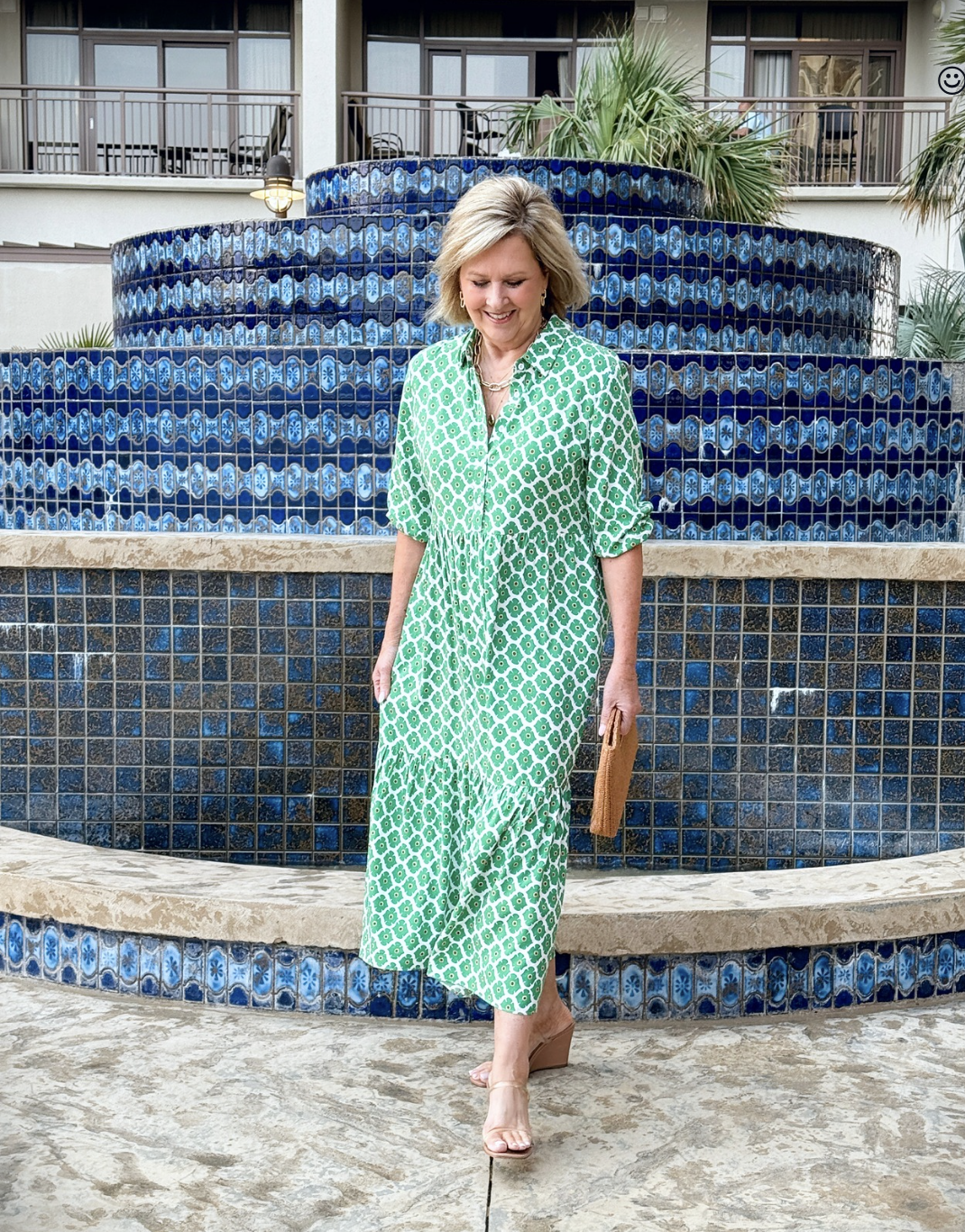 Woman in green printed maxi dress laughing while walking on a beach boardwalk, skirt swirling around her ankles like a movie star.